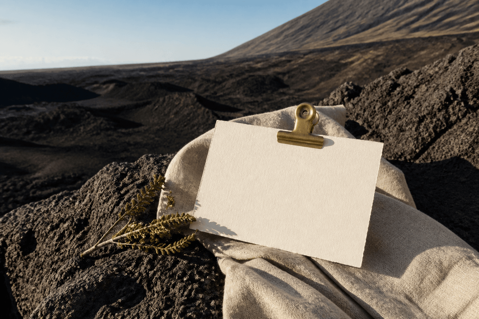 A blank unused ivory card under a brass clip on a Kohala lava-stone pass in hard sun.